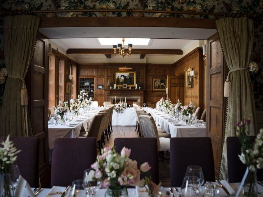 Elegant dining room with wood paneling, floral centerpieces, white table linens, and classic chandelier, set for a formal event