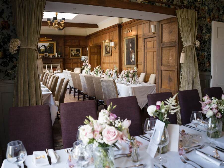 Elegant dining room with long tables set for event, floral centerpieces, wooden paneled walls, classic paintings, and soft lighting