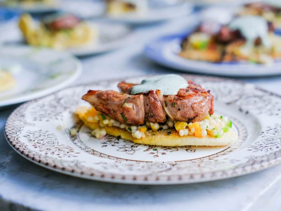 Grilled meat topped with herb sauce served on a bed of pearl couscous and vegetables on a decorative plate