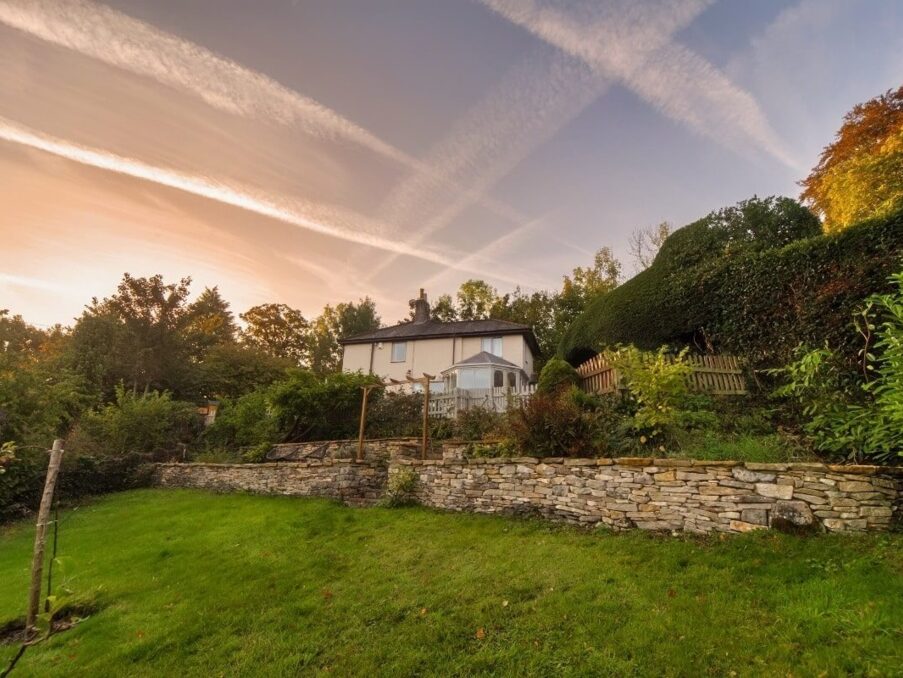 Cozy countryside guesthouse with stone terraced garden, lush greenery, and a tranquil sunset sky overhead