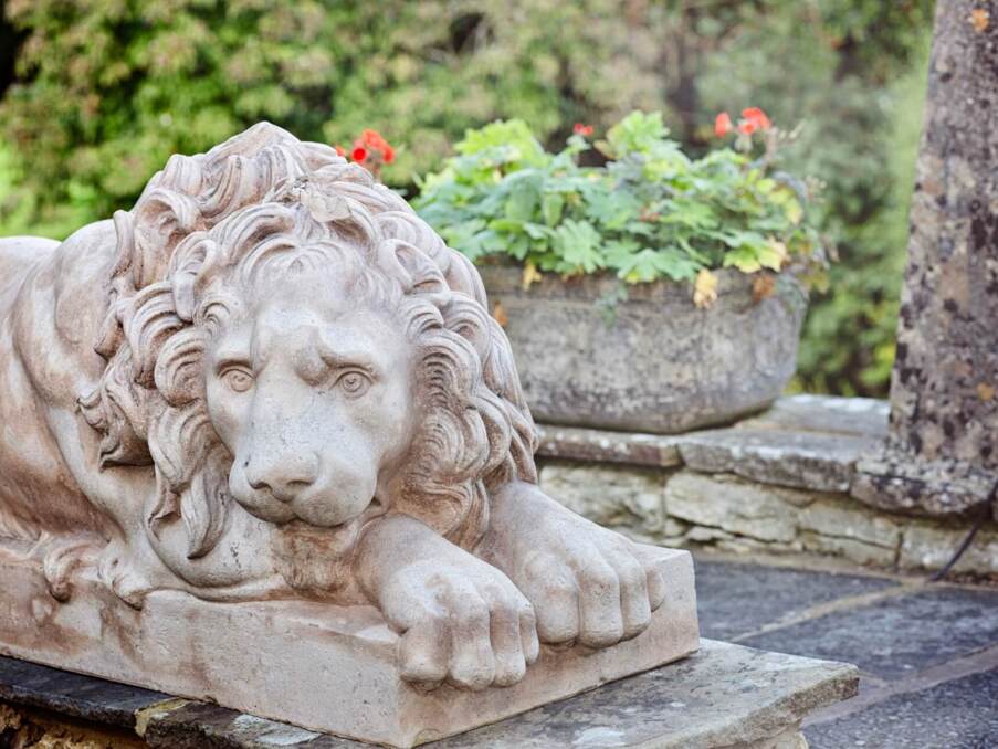 Detailed stone sculpture of a reclining lion in the hotel garden, near a stone planter with green and red flowers