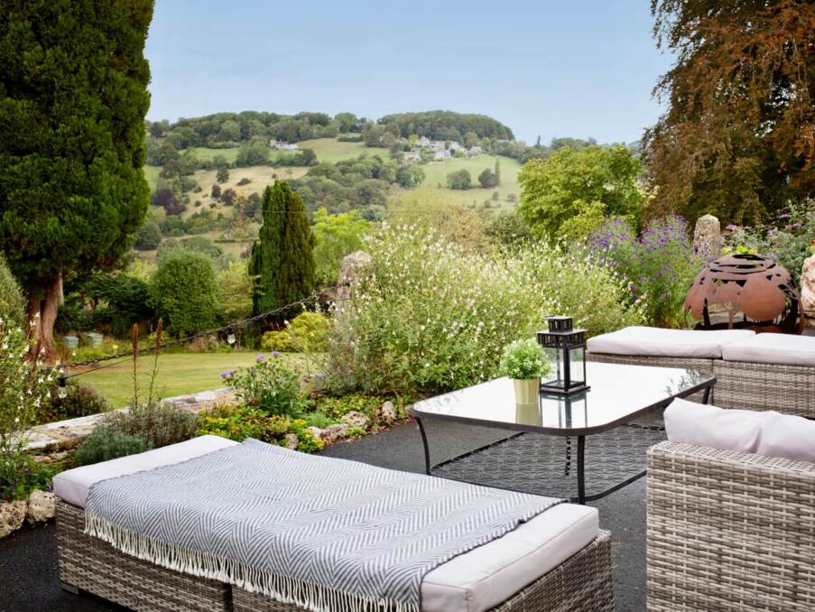 Outdoor patio with cushioned wicker seating, glass coffee table, decorative lantern, and scenic hillside views surrounded by lush greenery