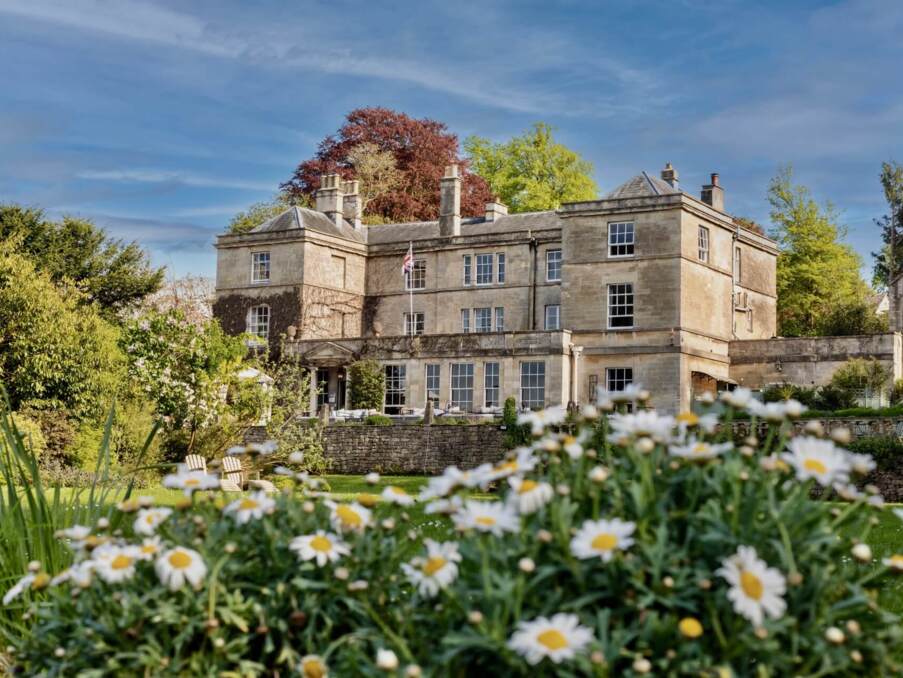 Historic stone country house hotel surrounded by lush gardens and blooming daisies under a clear blue sky