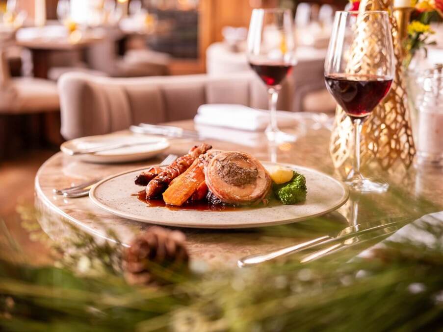 Gourmet meal with roasted meat, carrots, broccoli, and wine glass on a marble table in a cozy restaurant setting