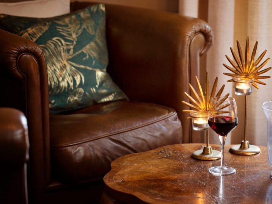 Cozy leather armchair with decorative pillow beside wooden table holding wine glass and elegant candle holders