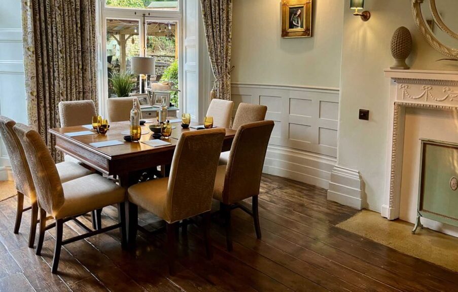 Elegant dining room with wooden table set for eight, comfortable upholstered chairs, hardwood floors, and a decorative fireplace.