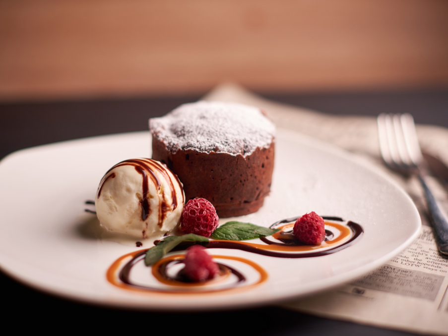 Warm chocolate lava cake dusted with powdered sugar, served with vanilla ice cream, fresh raspberries, and decorative caramel and chocolate swirls