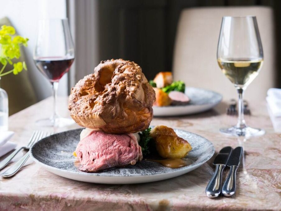 Elegant dining with roasted beef, Yorkshire pudding, side vegetables, paired with glasses of red and white wine on a marble table