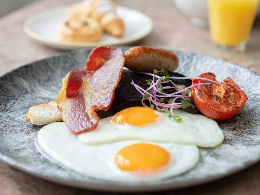 Plate with two sunny-side-up eggs, crispy bacon, sausage, grilled tomato, black pudding, and microgreens, part of a hotel breakfast