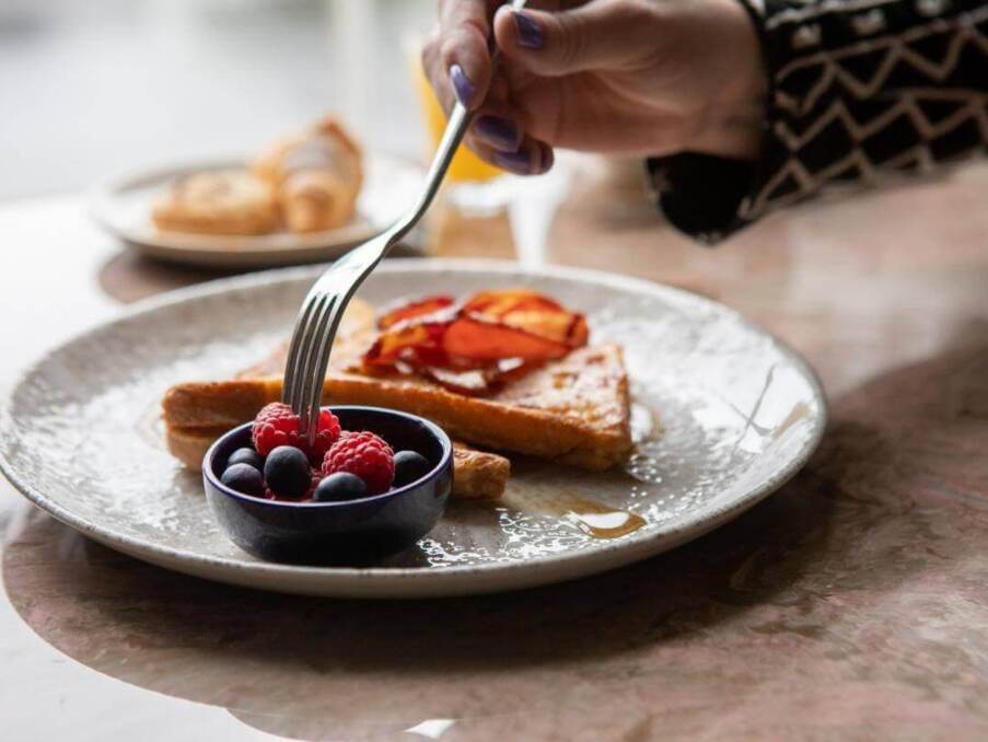 Breakfast plate with French toast topped with crispy bacon, served with fresh raspberries and blueberries in a small dish