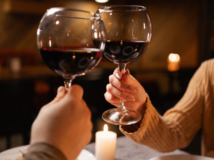 Two guests toasting with red wine glasses at a candlelit table with gourmet dishes in a cozy restaurant ambiance
