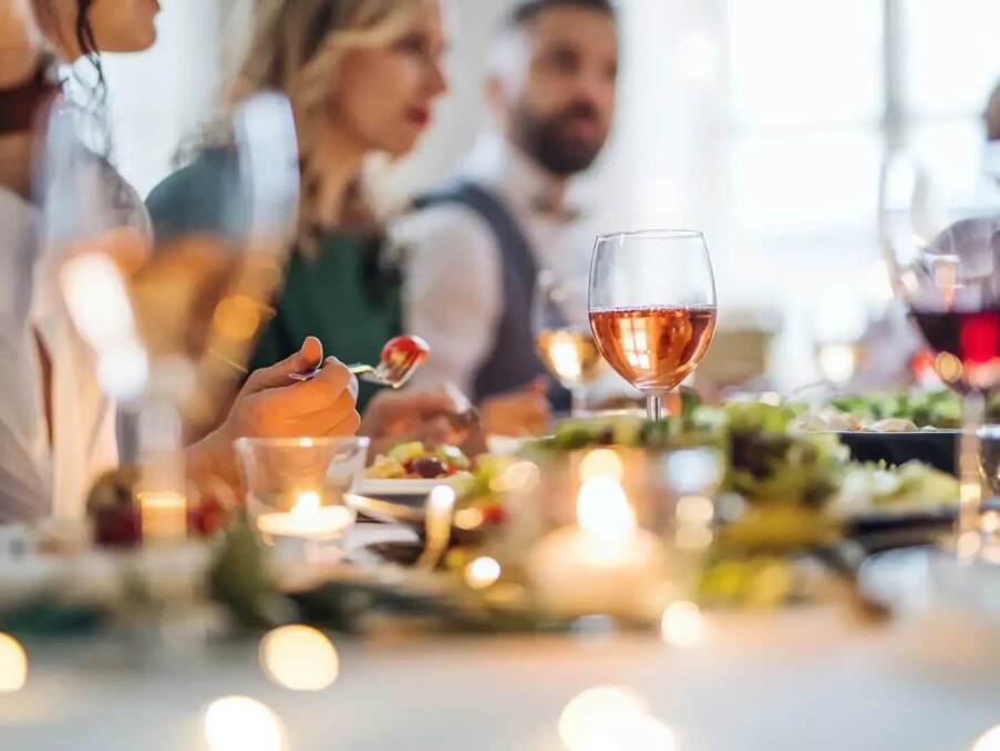 Guests enjoying a warm, candlelit dinner with wine glasses and fresh food on a softly decorated dining table