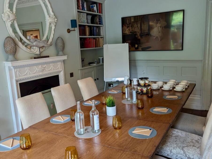 Elegant meeting room with a large wooden table set for a conference, cushioned chairs, decorative mirror, chandelier, and refreshments