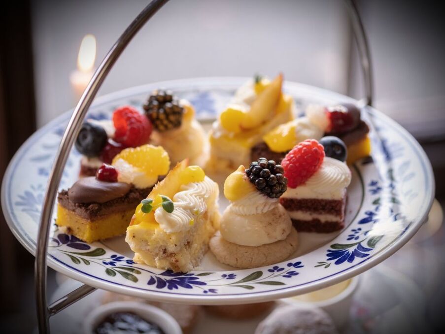 Assorted miniature pastries and fruit-topped petit fours on a decorative tiered plate, elegant afternoon tea presentation