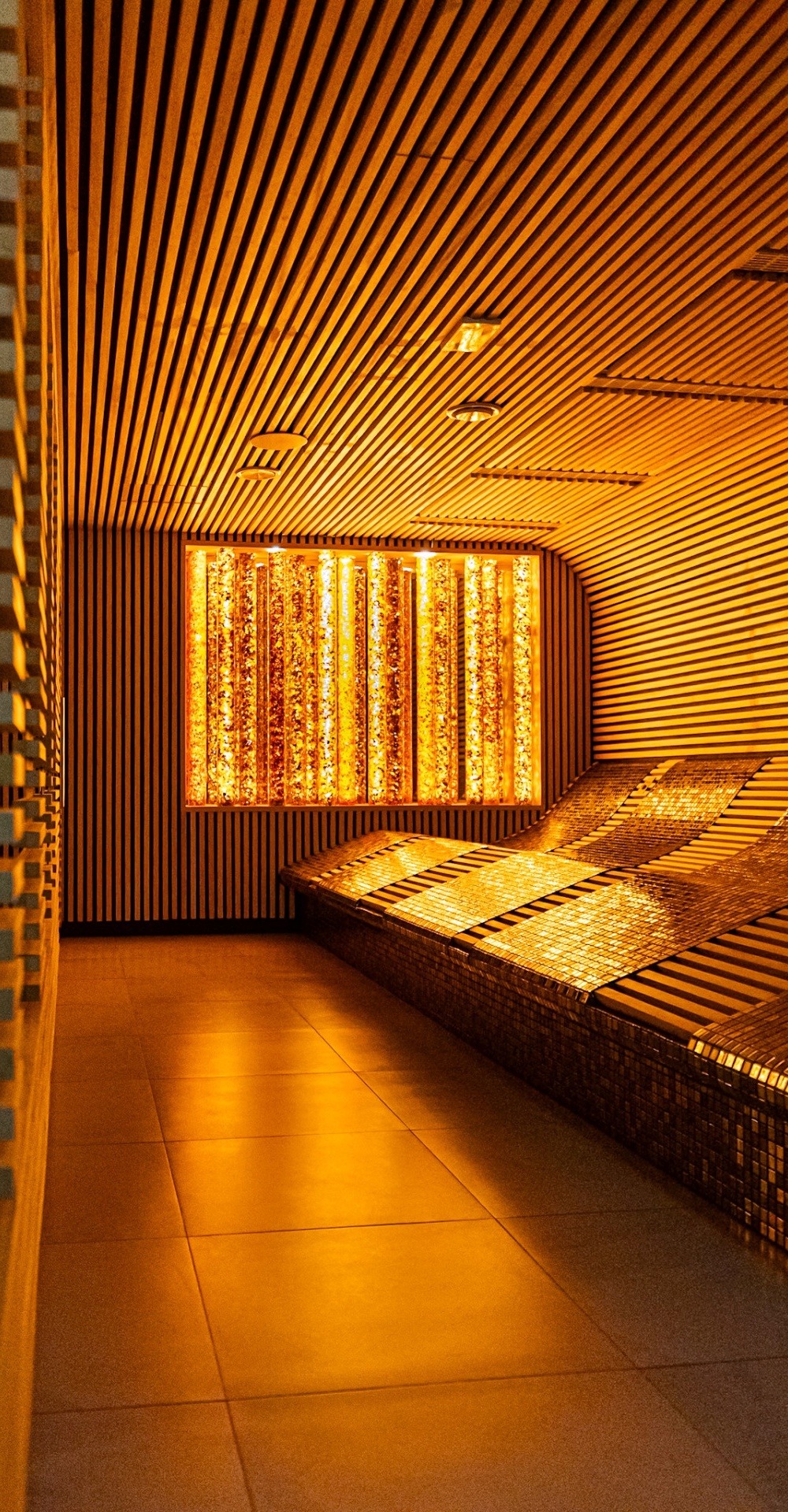 Przytulne miejsce relaksu w spa z podświetlanymi, wyprofilowanymi leżankami i nowoczesnym drewnianym wykończeniem ścian i sufitu