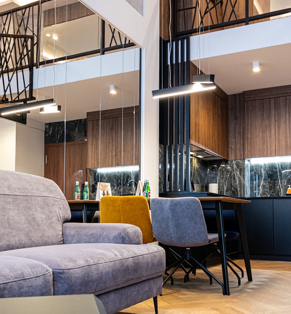 Nowoczesny apartament z otwartą kuchnią, jadalnią i szarą sofą, drewnianymi schodami i designerskim oświetleniem