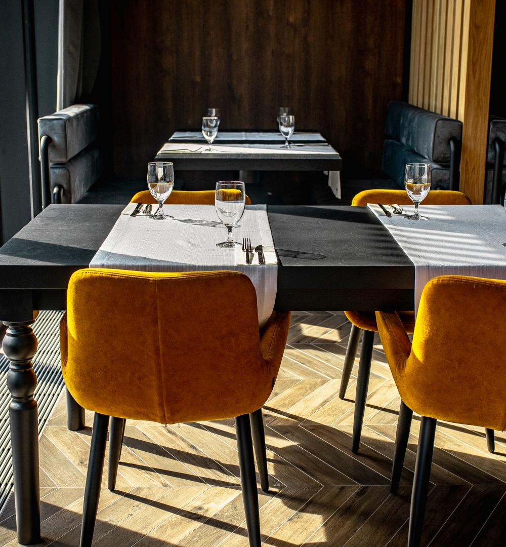 Nowoczesna restauracja z czarnymi stołami, pomarańczowymi krzesłami, białymi obrusami i dużymi oknami wpuszczającymi światło