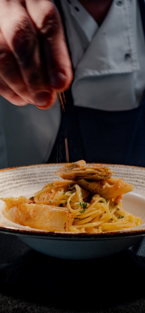 Szef kuchni dekoruje danie z makaronu tagliatelle z przyprawami w profesjonalnej kuchni hotelowej