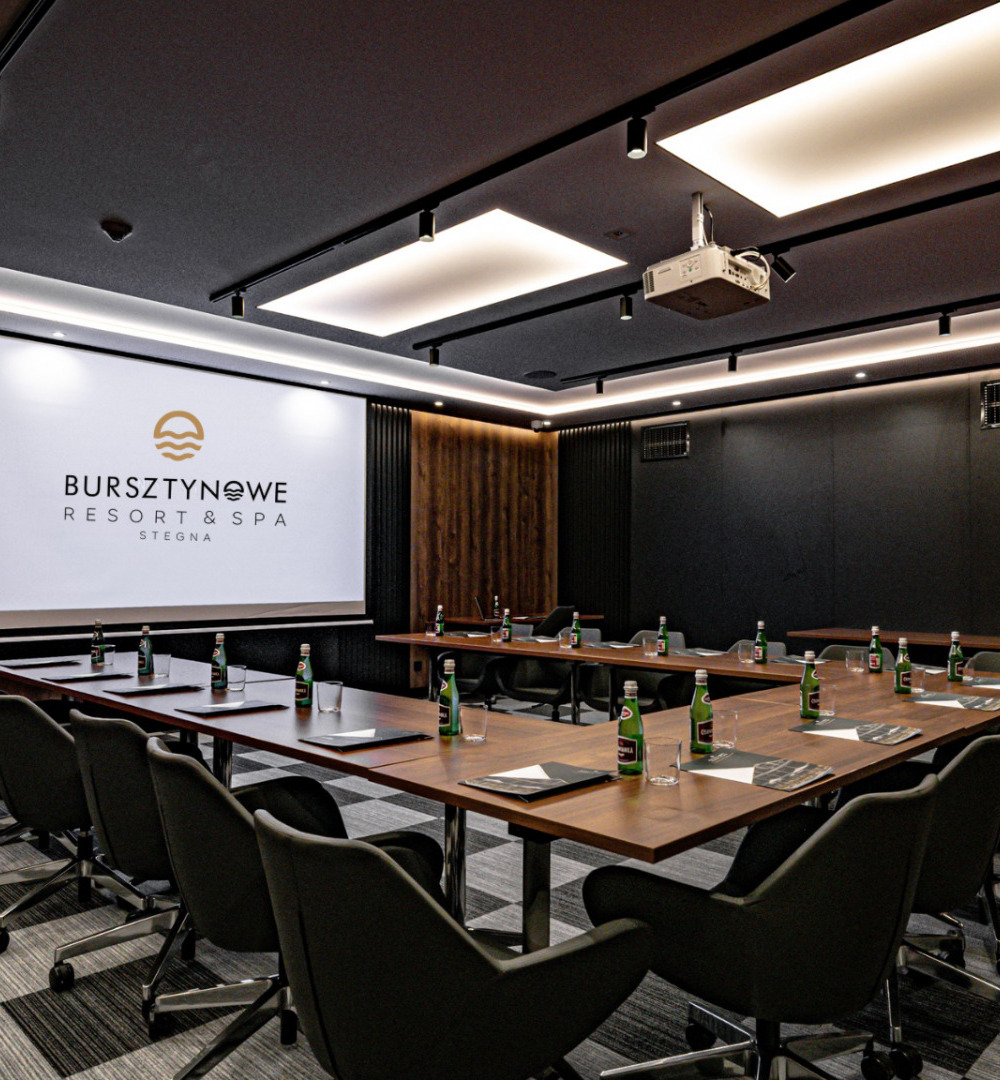 Nowoczesna sala konferencyjna z drewnianymi panelami, dużym ekranem i wygodnymi fotelami na kółkach w Bursztynowe Resort & Spa.