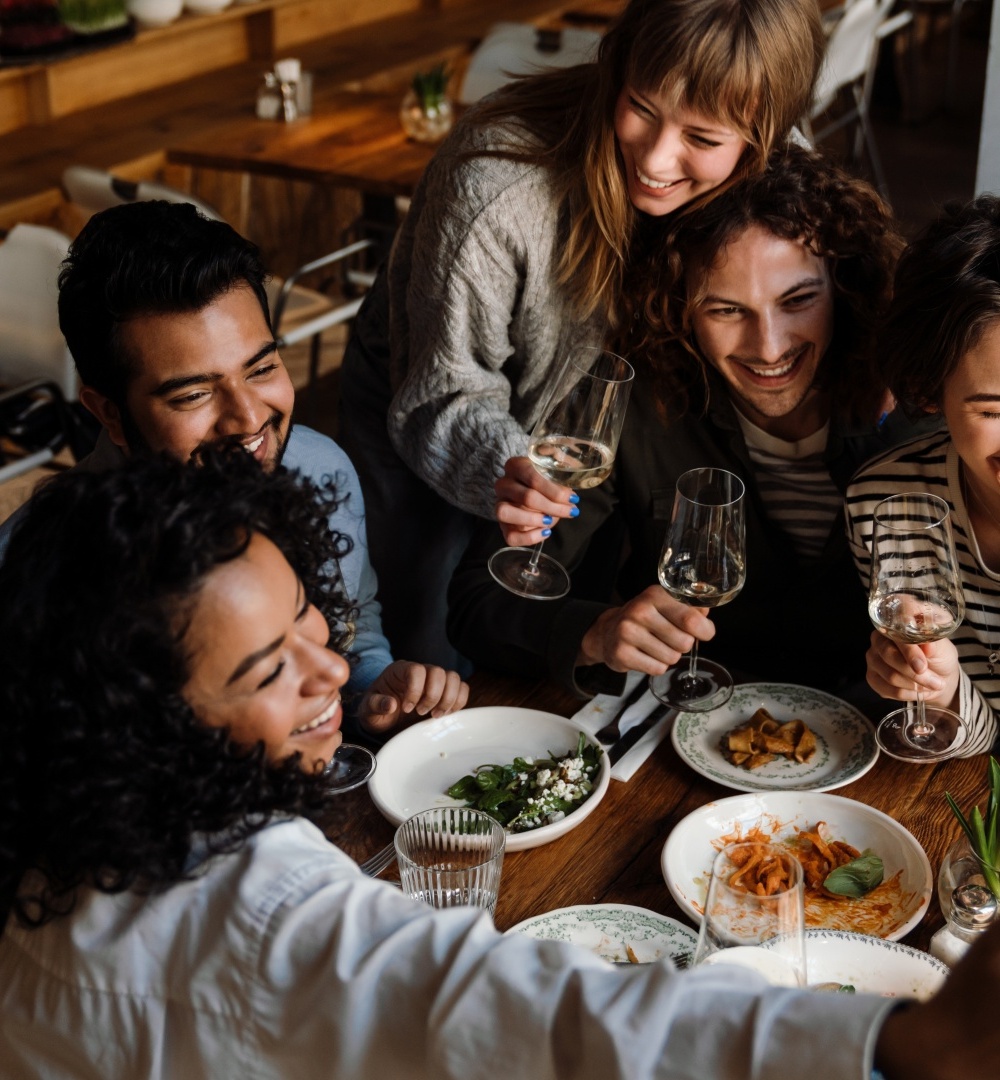 Grupa przyjaciół w przytulnej restauracji robiąca selfie przy stole z przekąskami i kieliszkami z winem.