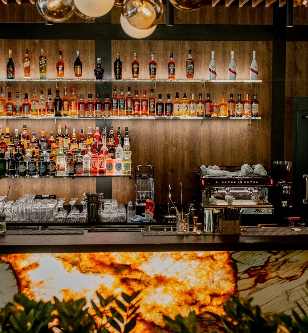 Elegancki bar hotelowy z podświetlanym blatem, pełną kolekcją alkoholi, szkłem do napojów i ekspresem do kawy