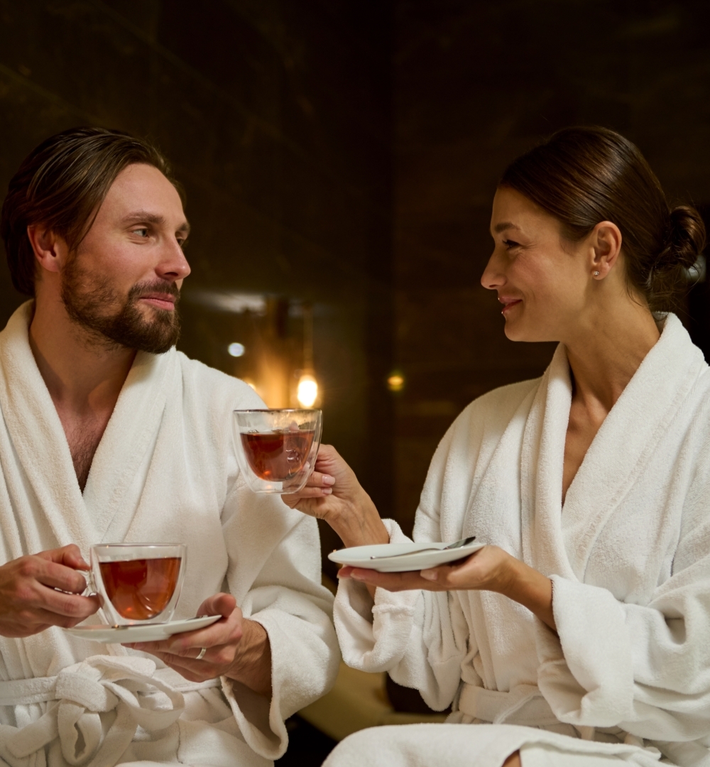 Para w białych szlafrokach relaksuje się w spa, pijąc gorącą herbatę w nastrojowym, przytulnym wnętrzu.