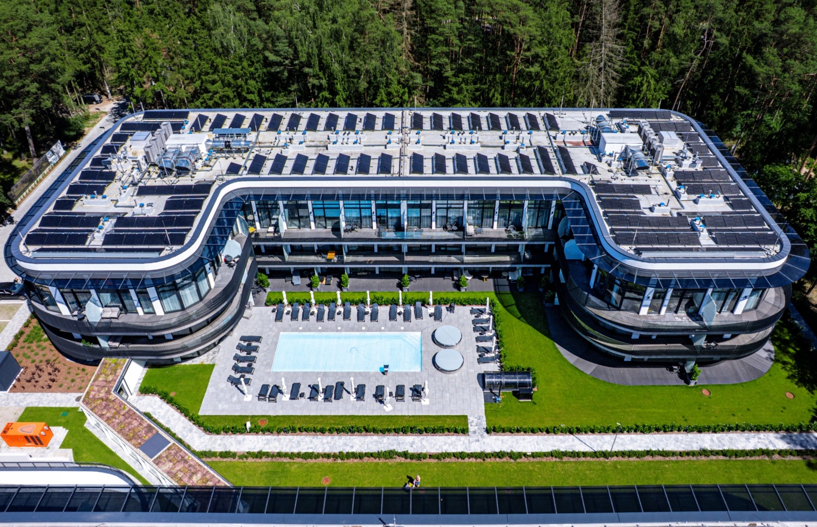 Nowoczesny hotel z basenem na świeżym powietrzu i tarasami, otoczony zielonym lasem, idealny na relaks i wypoczynek.