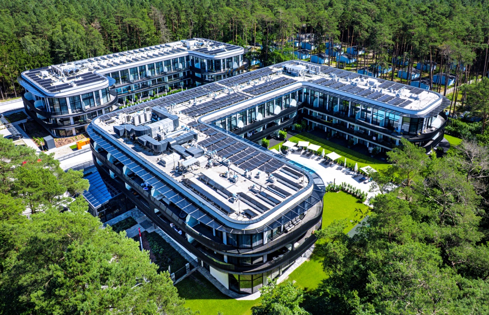 Nowoczesny hotel z trzema piętrami otoczony lasem, z basenem, dużymi oknami i przestronnym ogrodem