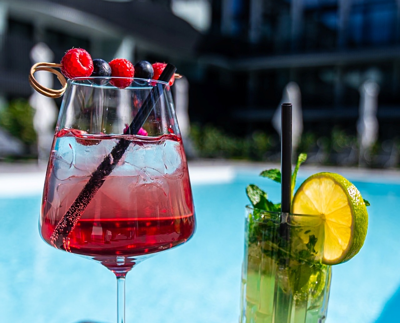 Kolorowe koktajle z owocami i miętą na stoliku przy basenie hotelowym w nowoczesnym budynku na tle błękitnego nieba