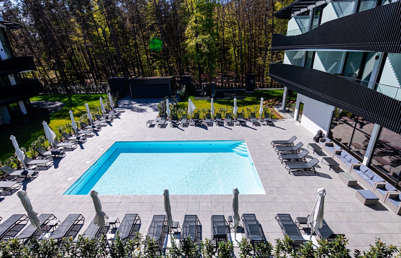 Nowoczesny hotel z basenem na dziedzińcu, otoczony leżakami i parasolami, w otoczeniu zieleni i lasu