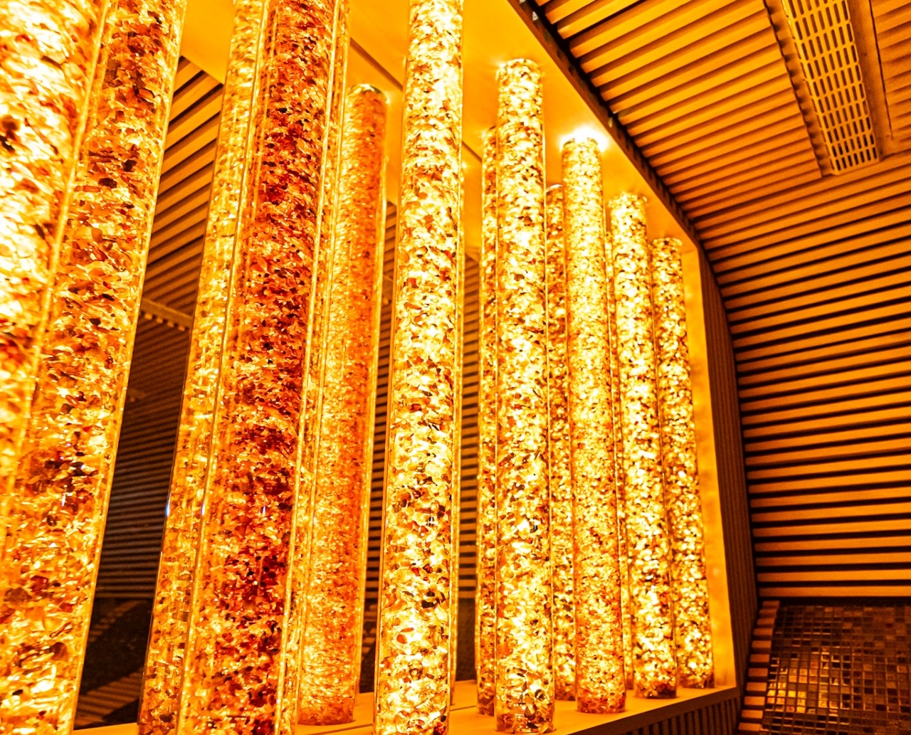 Ciepłe, złote słupki świetlne tworzące relaksującą atmosferę w nowoczesnym spa hotelowym z mozaikową ławką.