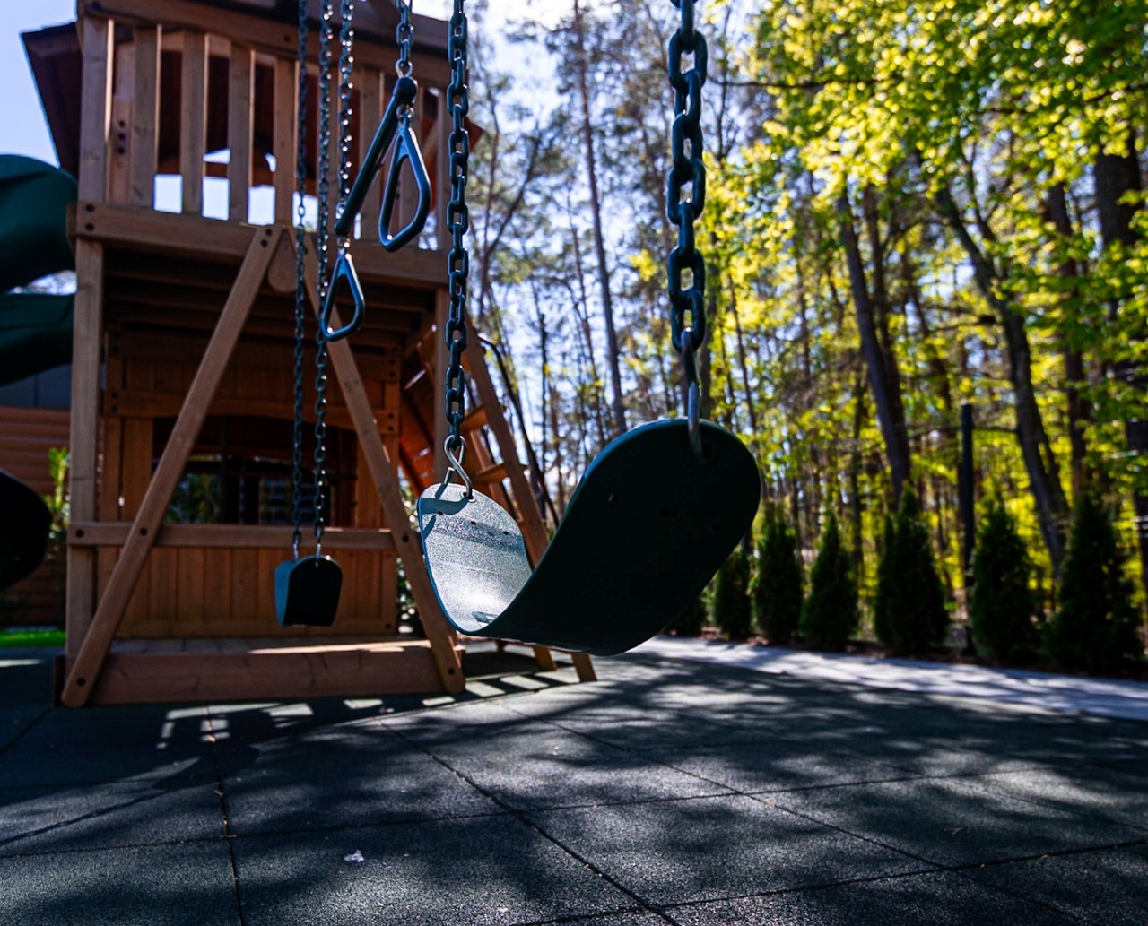 Plac zabaw z huśtawkami i drewnianą wieżą, otoczony zielonym lasem, idealny dla rodzin z dziećmi w hotelu