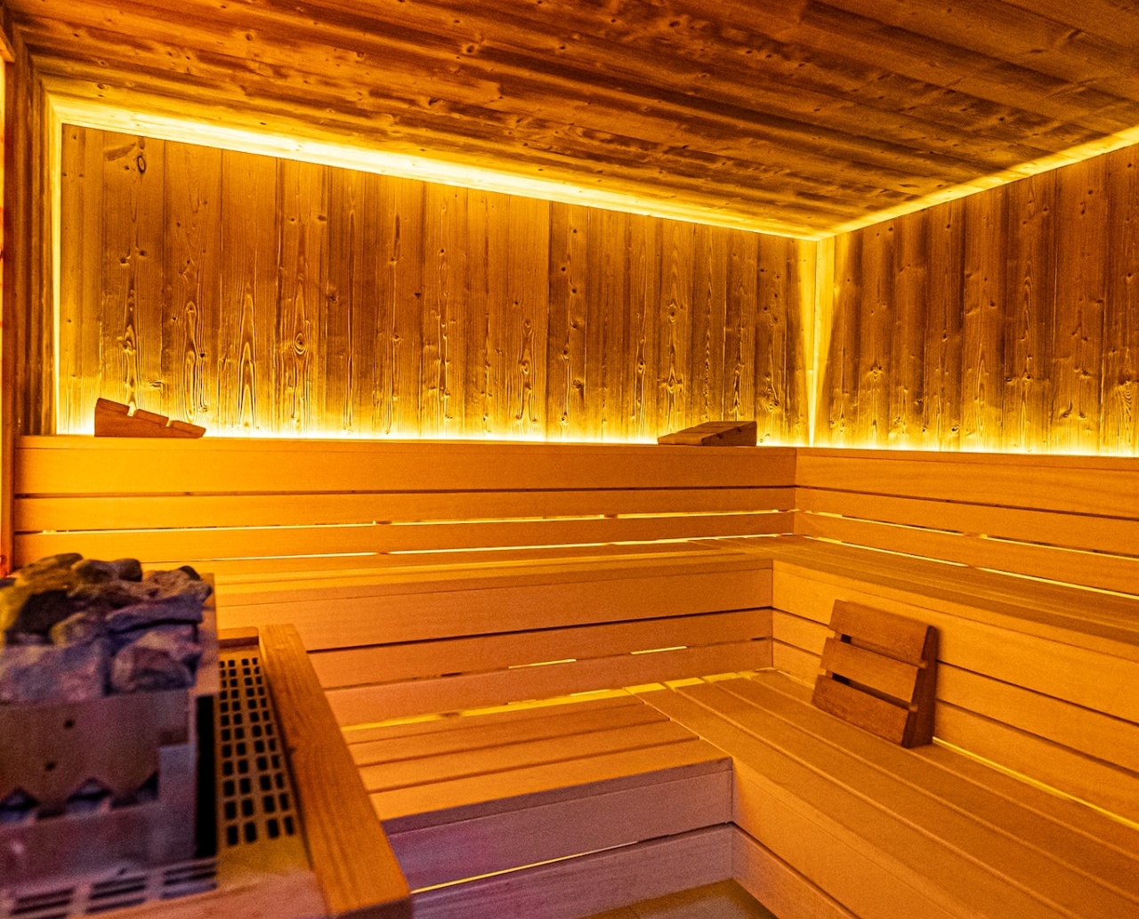 Przytulna sauna z drewnianymi ławami, kamieniami do sauny i ciepłym, nastrojowym oświetleniem LED