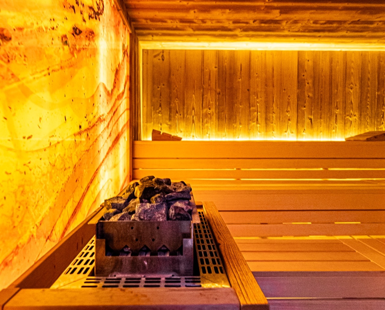 Przytulna sauna z drewnianymi ławkami, kamieniami do pary i ciepłym, ambientowym oświetleniem dla relaksu gości.