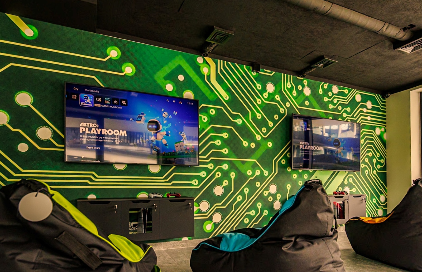 Nowoczesny pokój rozrywki hotelowej z telewizorami do gier, wygodnymi pufami i ścianą ozdobioną wzorem obwodów elektronicznych
