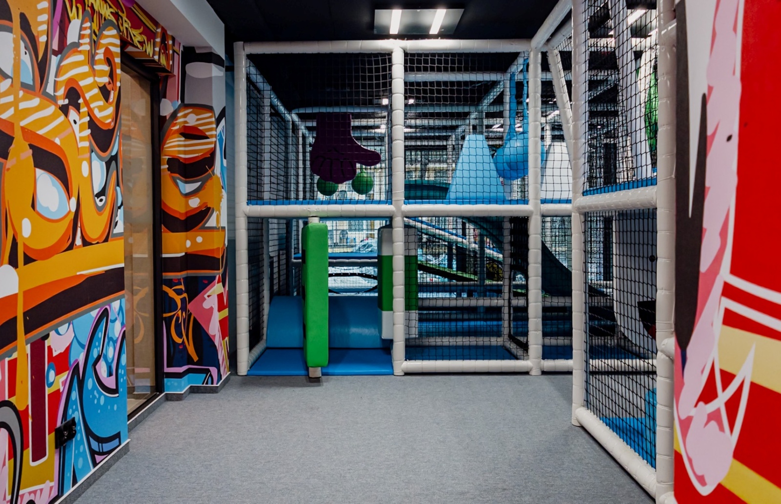 Kolorowy, bezpieczny plac zabaw dla dzieci w hotelu, z miękkimi przeszkodami i ścianami pokrytymi muralami graffiti.