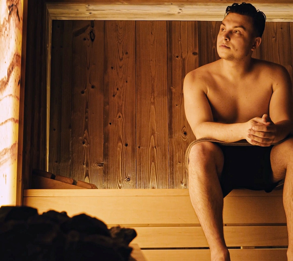 Mężczyzna odpoczywający w drewnianej saunie hotelowej z ciepłym oświetleniem i naturalnym wnętrzem