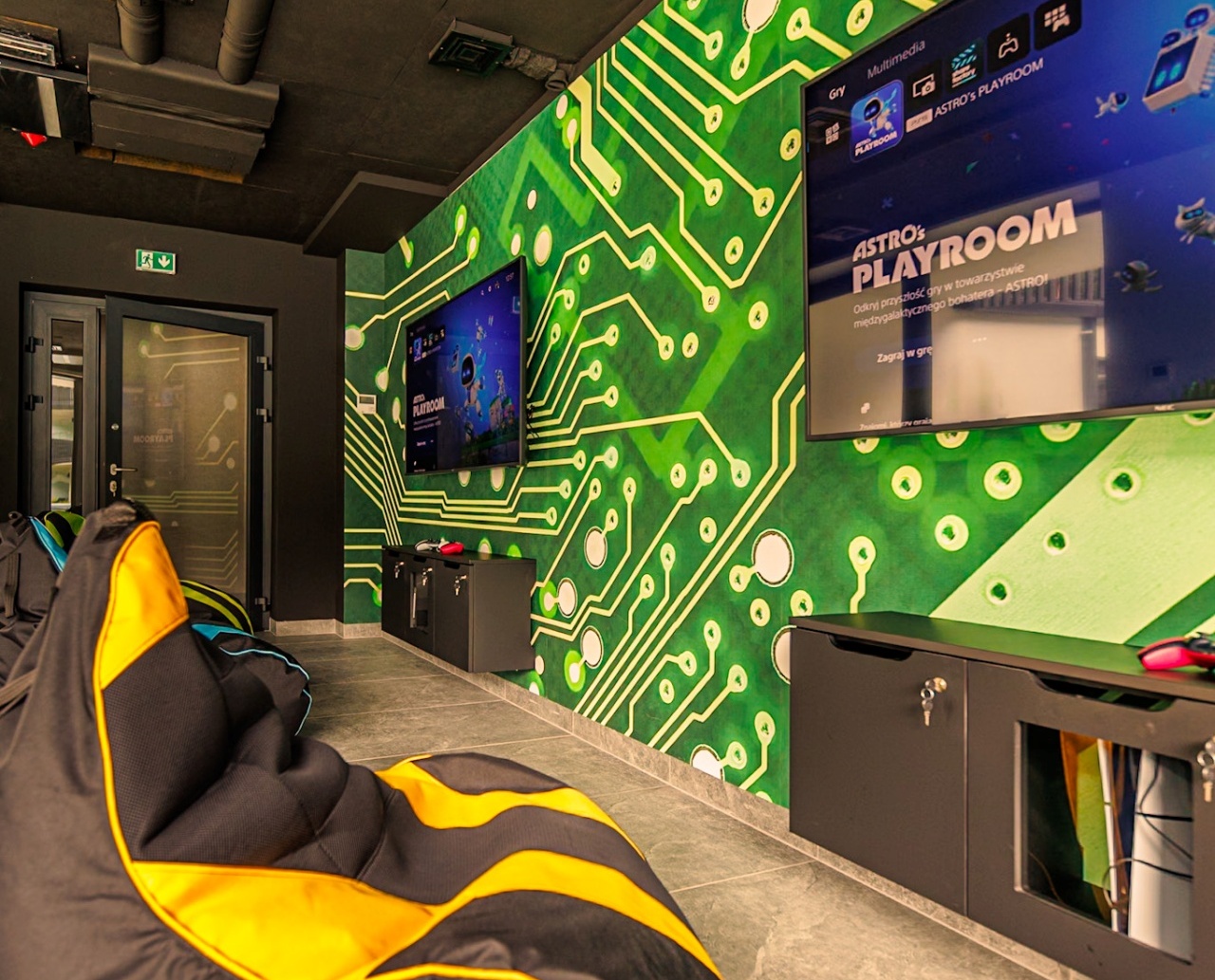 Pokój do gier z wygodnymi pufami, dużymi ekranami TV i ścianą ozdobioną wzorem obwodów elektronicznych