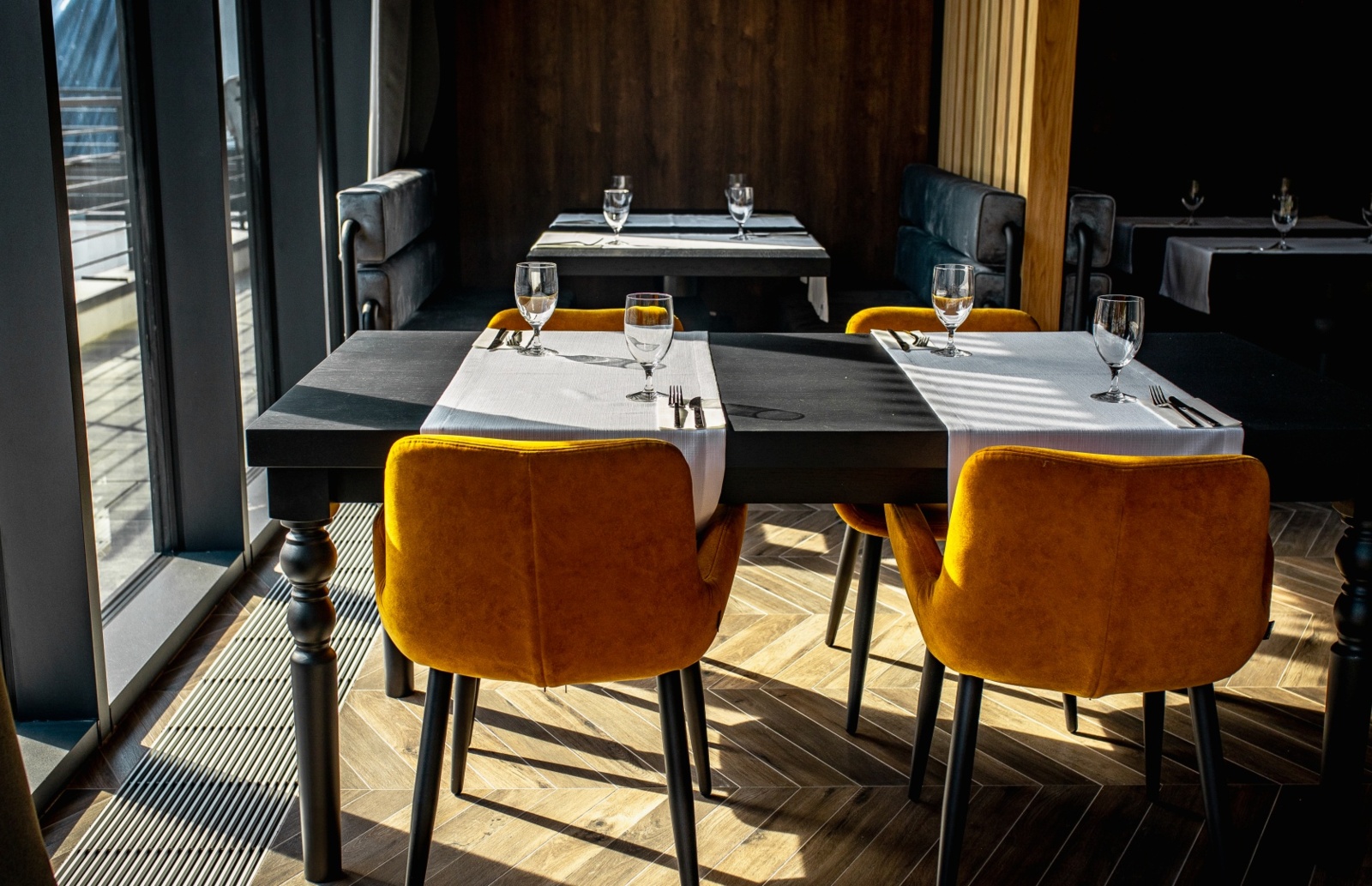 Nowoczesna restauracja z czarnymi stołami, pomarańczowymi krzesłami, białymi obrusami i dużymi oknami wpuszczającymi światło