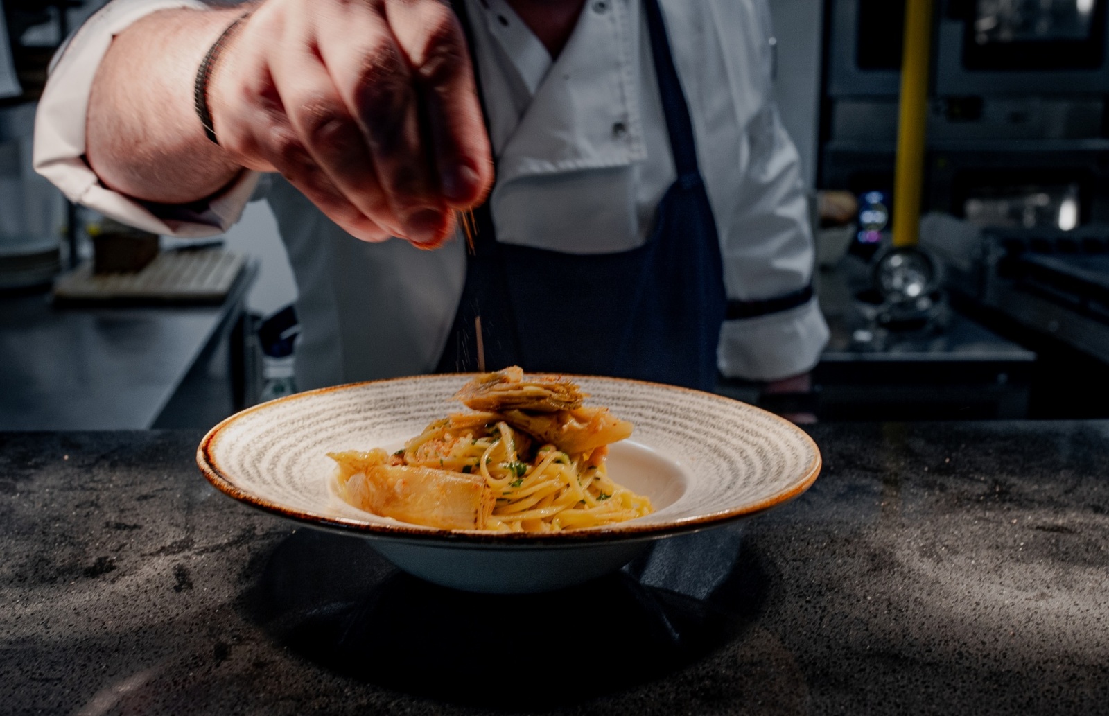 Szef kuchni dekoruje danie z makaronu tagliatelle z przyprawami w profesjonalnej kuchni hotelowej