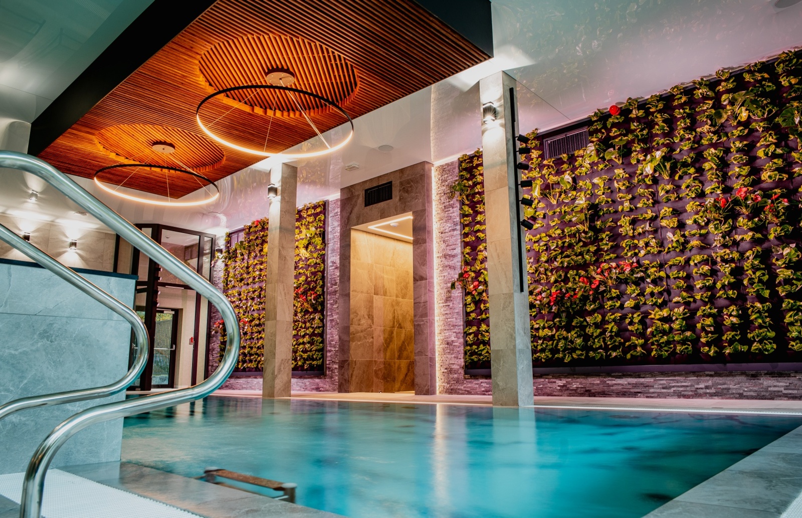 Ekskluzywny, kryty basen hotelowy z nowoczesnym oświetleniem i ścianami z roślin ozdobnych tworzącymi relaksującą atmosferę