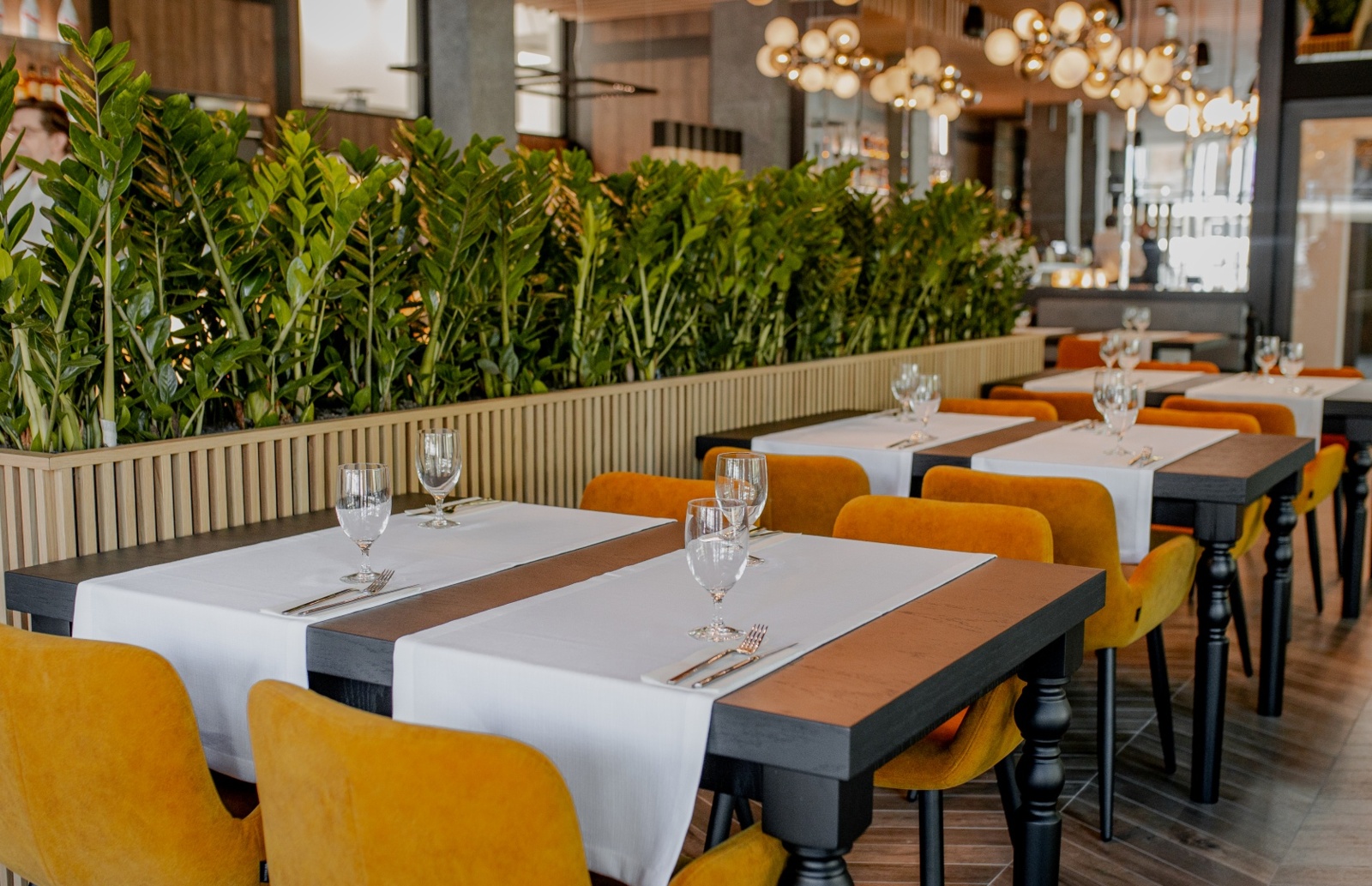 Nowoczesna restauracja hotelowa z eleganckimi stołami, żółtymi krzesłami i zielonymi roślinami tworzącymi przytulną atmosferę