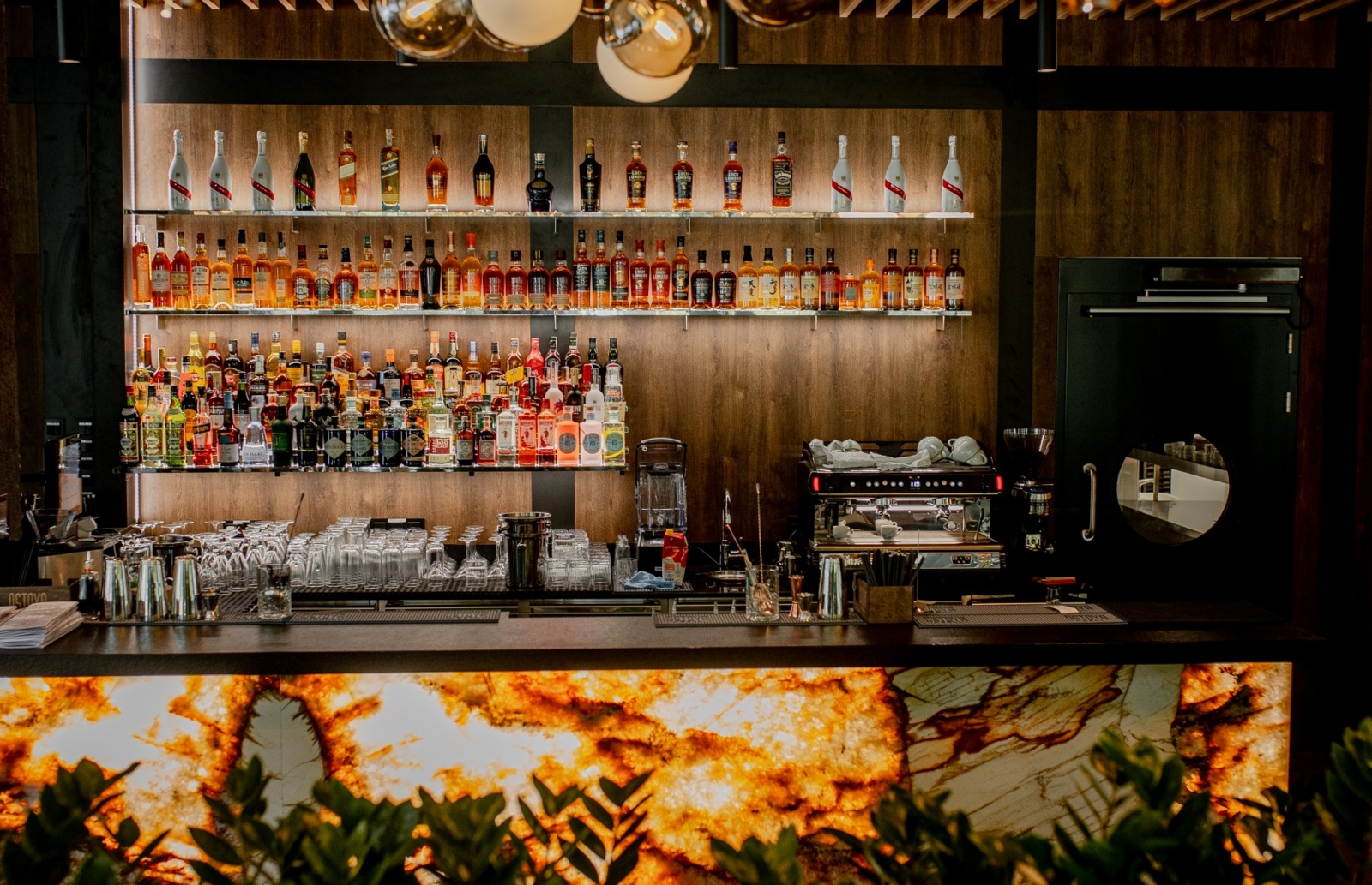 Elegancki bar hotelowy z podświetlanym blatem, pełną kolekcją alkoholi, szkłem do napojów i ekspresem do kawy