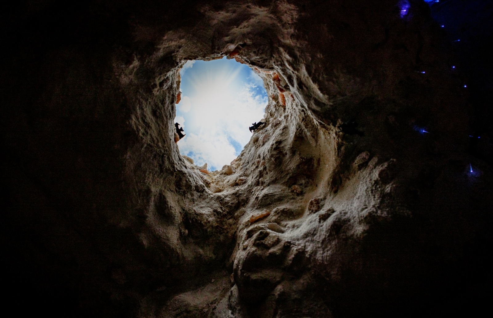 Widok nieba przez naturalne skalne okno w jaskini, z miękką teksturą skał i delikatnym światłem niebieskich punktów