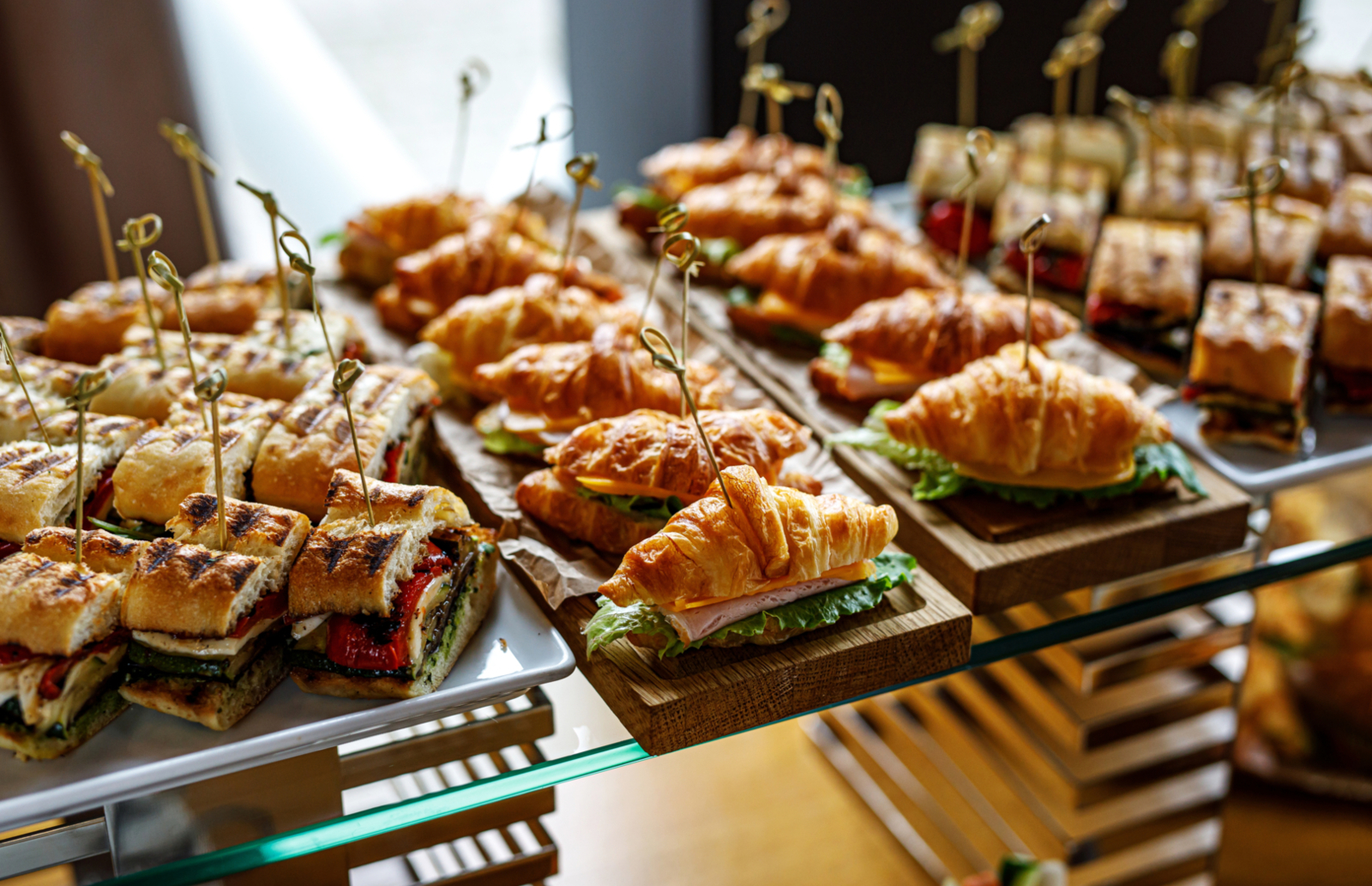 Zestaw mini kanapek z croissantami i ciabatą z warzywami i serem, starannie podane na drewnianych i porcelanowych tacach.