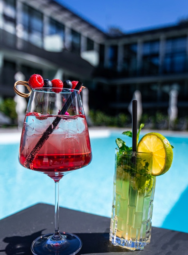 Kolorowe koktajle z owocami i miętą na stoliku przy basenie hotelowym w nowoczesnym budynku na tle błękitnego nieba