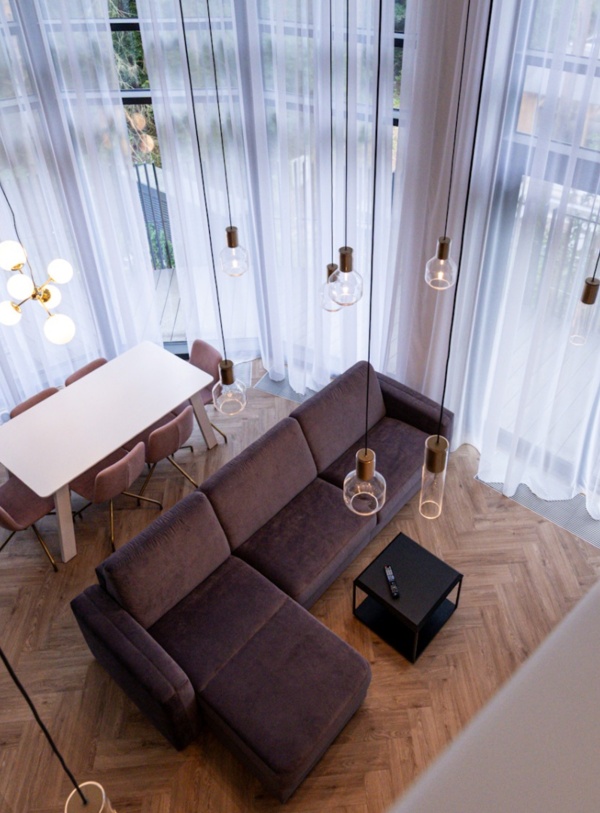 Nowoczesny apartament z dużym narożnym fioletowym narożnikiem, białym stołem i różowymi krzesłami przy oknach z przezroczystymi zasłonami