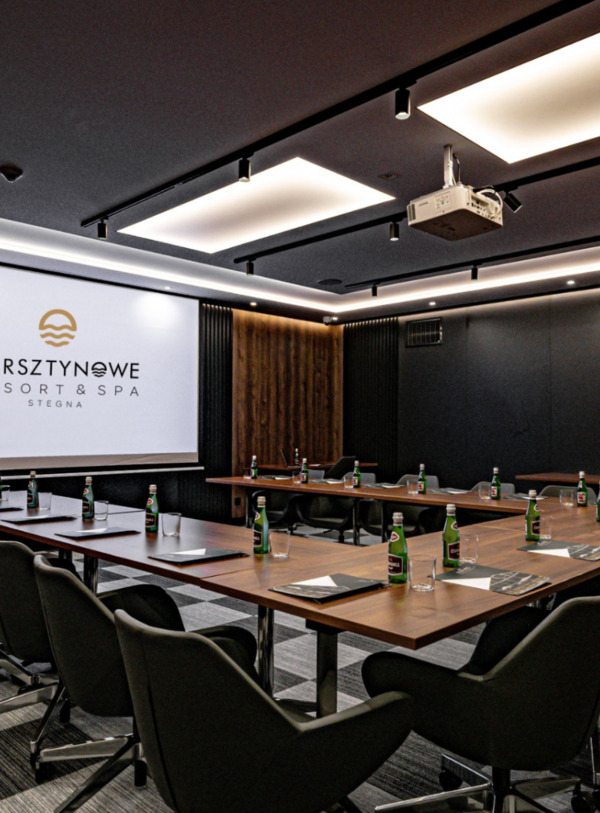 Nowoczesna sala konferencyjna z drewnianymi panelami, dużym ekranem i wygodnymi fotelami na kółkach w Bursztynowe Resort & Spa.