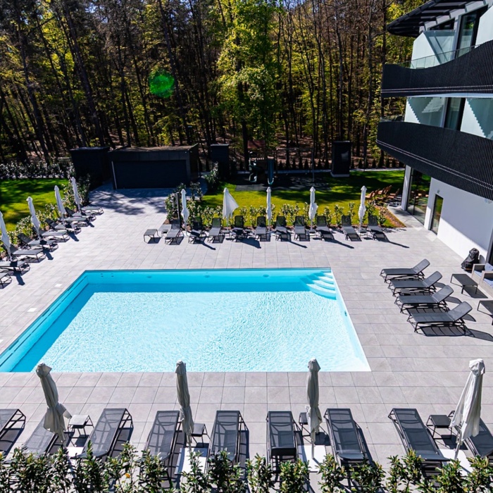 Nowoczesny hotel z basenem na dziedzińcu, otoczony leżakami i parasolami, w otoczeniu zieleni i lasu