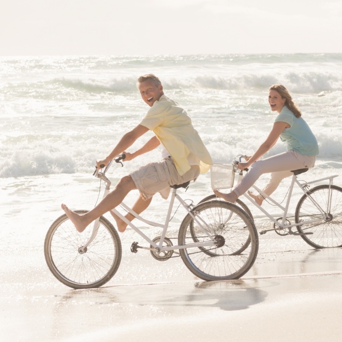 Para na rowerach jedzie brzegiem morza na piaszczystej plaży w słoneczny dzień, ciesząc się wakacyjną atmosferą